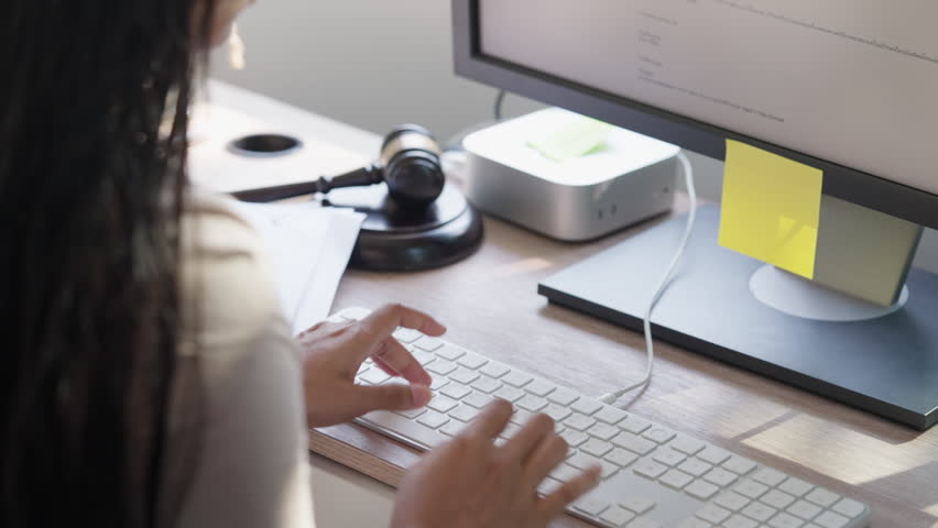 Lawyer typing on keyboard with judge gavel and computer in modern office, representing legal workflow, business law, digital technology, and professional corporate legal services concept.