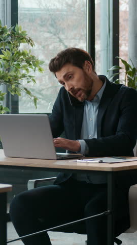 Busy Caucasian business man in office typing laptop talking mobile phone quarrel professional male manager multitasking discussing cellphone arguing client dissatisfied businessman guy writing notes