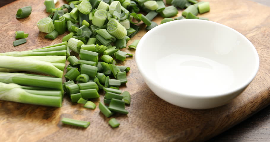 Woman putting pieces of fresh green onion into bowl at wooden table, closeup