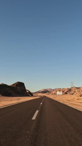 Vertical shot of pov driving through asphalt desert road with rocky slopes on roadside at sunset