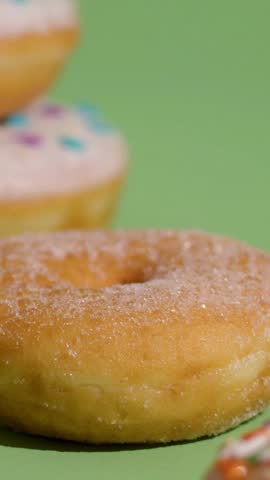 Fine white sugar being sprinkled over a fresh golden donut on a bright green background in slow motion close up view