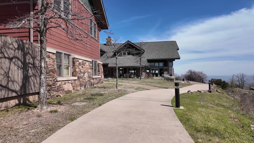 A large rustic style building with stone and wood construction sits atop a hill, featuring a wide paved pathway leading to its entrance of The Lodge at Mount Magazine.