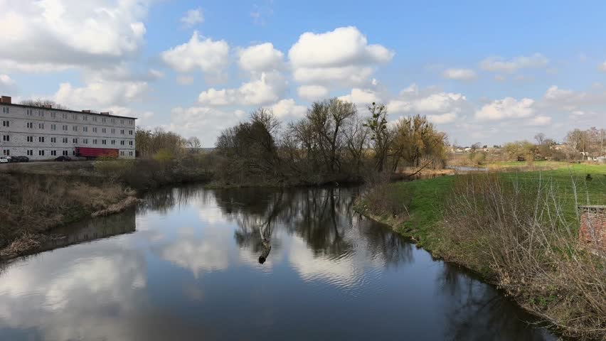 Scenic view of a calm river winding through a rural landscape with vibrant green grass and beautiful cloud formations.