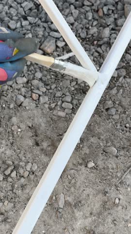 A vertical perspective of a white tubular metal construction possibly a greenhouse or tent frame standing on gravel soil