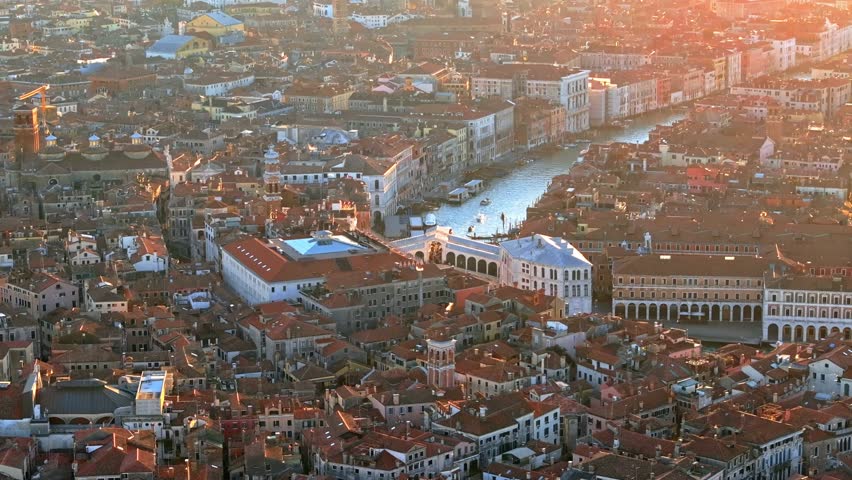 Aerial view of Venice city skyline at sunset showing grand canal and rialto bridge with orange light.