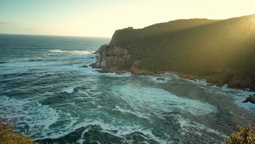 Dramatic Coastal Landscape Showcasing Sunset Glow Illuminating Jagged Rocks And Lush Flora