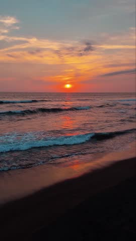 Beautiful Sunset Over the Ocean with Waves Crashing on Dark Sand Beach. Golden Sun Disc on the Horizon with Vibrant Orange Sky Background.