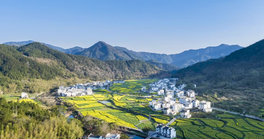 Aerial time-lapse of rapeseed flower fields patches weave between white Huizhou-style villages in spring valley, Wuyuan County, Jiangxi Province, China