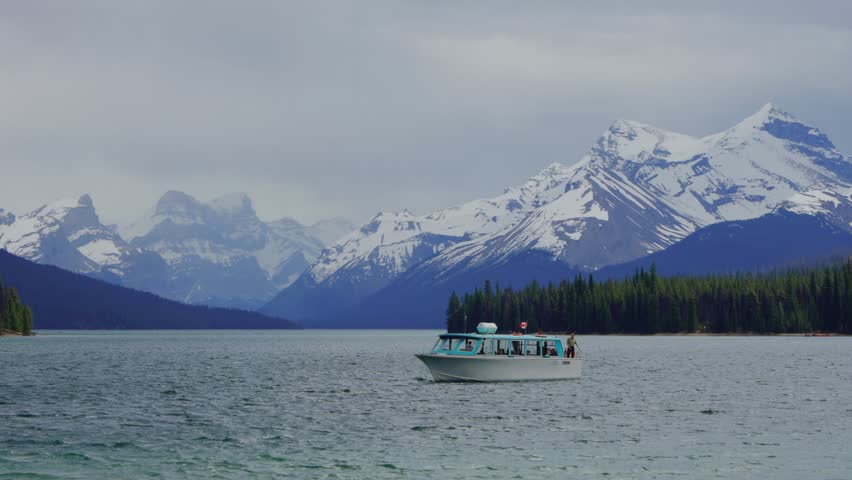 Tourist boat cruising Maligne Lake with snow capped mountains in Jasper national park, Canada