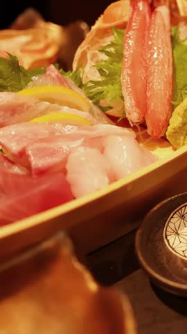 Soy sauce pours from a ceramic pot into small dishes next to fresh seafood sashimi