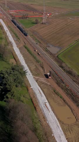 Aerial drone view of a high-speed passenger train moving through the countryside next to a railway line construction site with earthworks