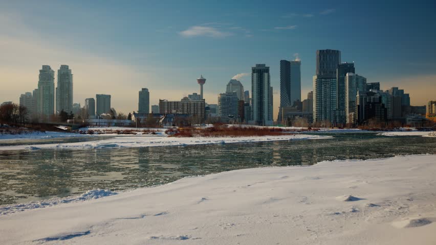 A beautiful daytime winter view of the downtown Calgary skyline in Alberta Canada. City towers and the Calgary Tower stand tall behind the icy Bow River and banks covered in fresh bright snow.
