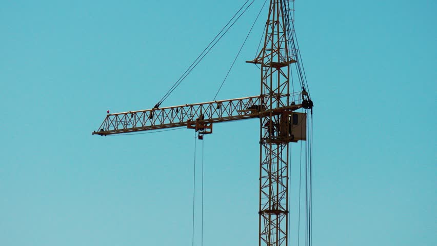 Two large cranes stand tall against the blue sky. They are positioned at a construction site