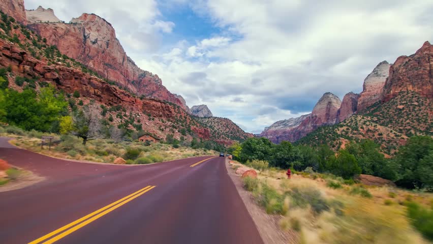 A view from a moving vehicle driving along the winding road through the stunning red rock canyons and towering sandstone cliffs of Zion National Park, Utah.