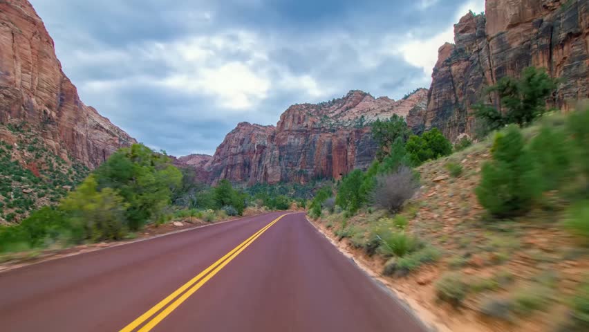 A dynamic, low-angle shot from a moving vehicle captures the stunning red rock canyon walls of Zion National Park along the Zion-Mount Carmel Highway (Route 9) in Utah, USA.