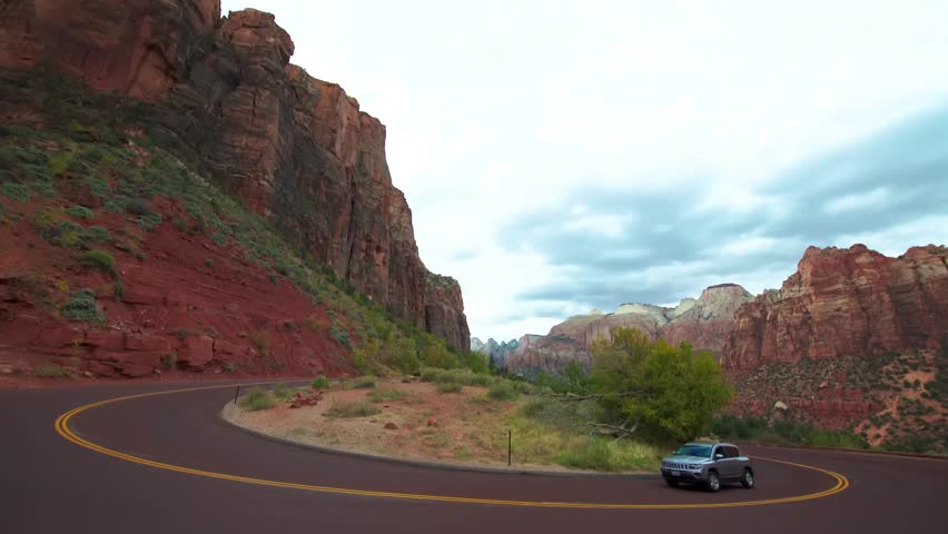 A car drives along a winding road through the dramatic red rock cliffs and canyons of Zion National Park in Utah, USA.