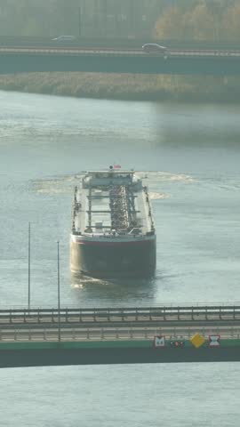 Maritime journey of an oil tanker navigating a bustling river with bridges and serene surroundings. Vertical video