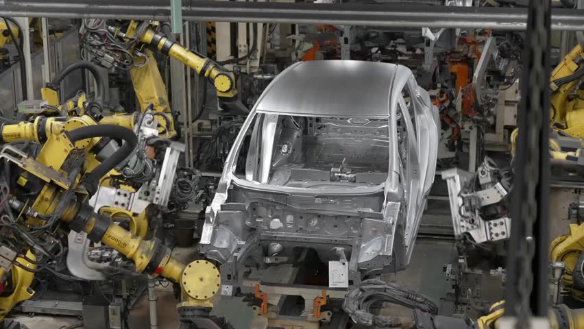 Wide shot of an automated workstation where several robotic arms converge to assemble a car body on an industrial conveyor