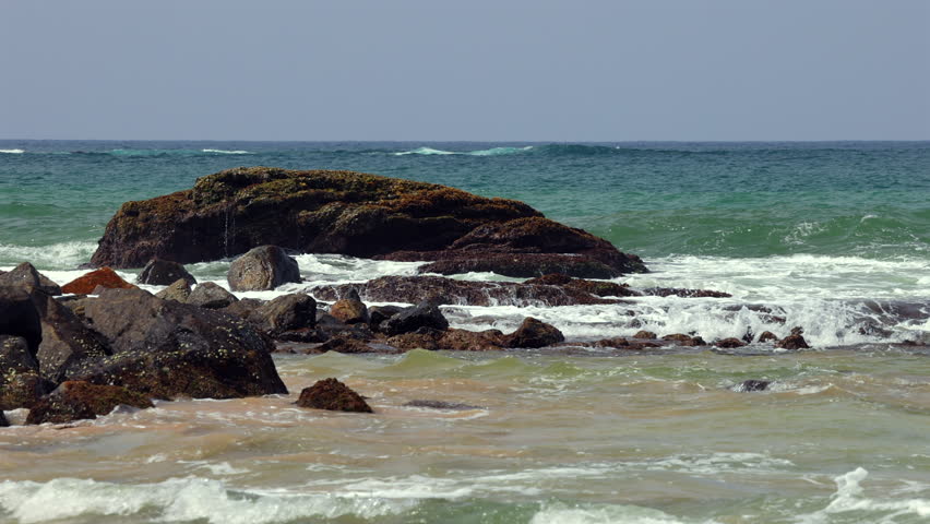 Ocean Waves Crash and Break Against Coastal Rocks and Sandy Beach Shoreline on a Bright Day with Blue Sky. Sri Lanka island in Asia.
