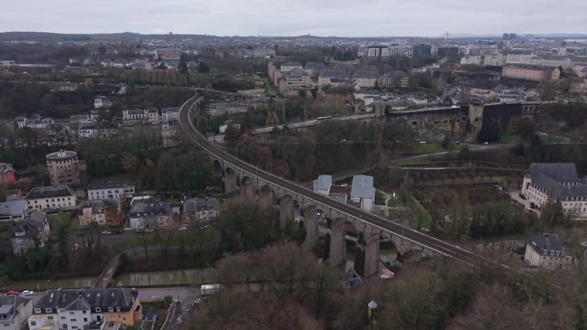 Drone footage of a stone railway bridge passing through a Luxembourg neighborhood, capturing urban streets, residential architecture, and historic infrastructure from above.