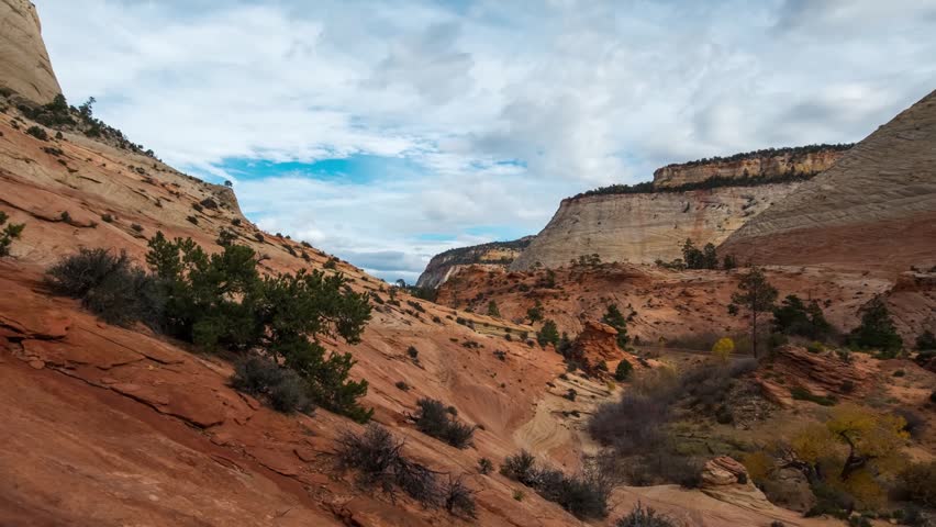 wide-angle shot of the iconic red rock formations and deep canyons of Zion National Park in Utah. The footage captures the dramatic contrast between the cream and orange Navajo sandstone cliffs, a bri