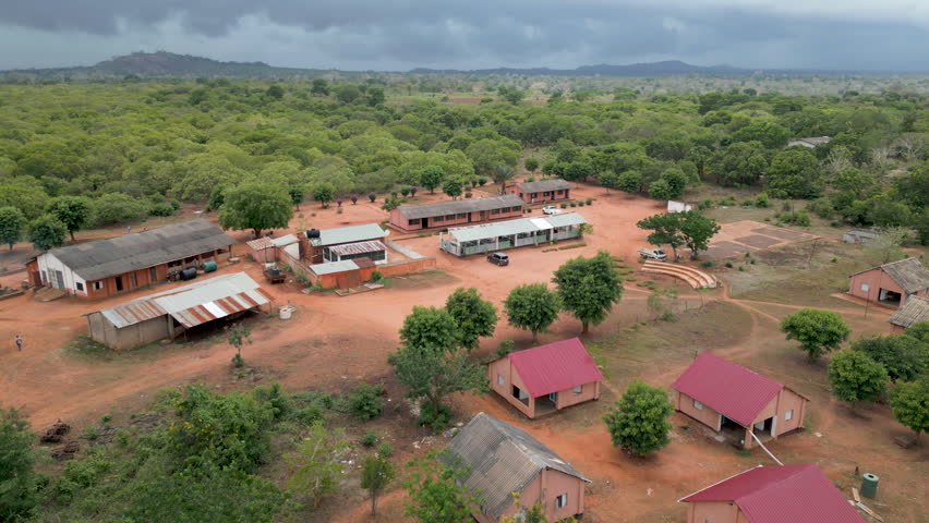 Aerial of a small rural village with buildings and small school surrounded by lush African wilderness.