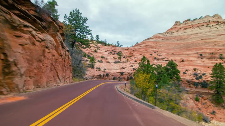 Footage of a vehicle driving along the winding Zion-Mount Carmel Highway (Utah State Route 9) through the stunning red rock canyon landscape of Zion National Park, Utah, USA.