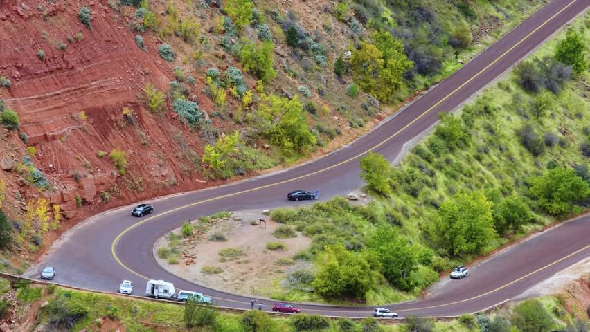 Aerial view of the famous switchbacks on the Zion-Mount Carmel Highway (State Route 9) in Zion National Park, Utah. The image captures vehicles, including cars and an RV, as they drive the dramatic, c