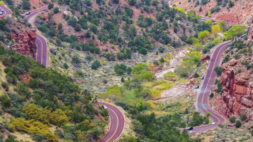 wide-angle view captures the dramatic, winding red asphalt of the historic Zion-Mount Carmel Highway (UT-9) cutting through the rugged, colorful landscape of Zion National Park, Utah.
