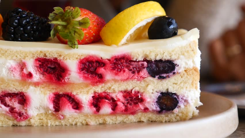 Delicious sponge cake with cream and fresh berries, cinematic food footage showing layers of fruit and sweet frosting.