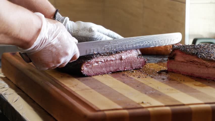 Slicer carves juicy lean Texas barbecue smoked brisket, carefeully slicing tender beef brisket for bbq plates, slow motion 4K