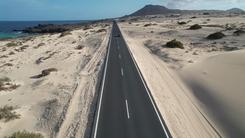 Aerial drone shot of empty straight road through sand dunes in Corralejo, wide and distant view. Minimalist desert landscape with symmetry and leading lines.