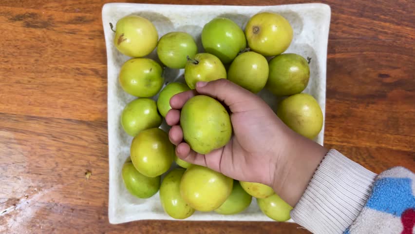 hand holding fresh green ber fruit over bowl of jujube on wooden table healthy seasonal fruit