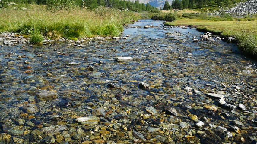Calm transparent waters of a mountain torrent at the famous Arpy Lake, Aosta Valley, Italy. Natural landscape with high peaks of italian alps on the background, with blue sky
