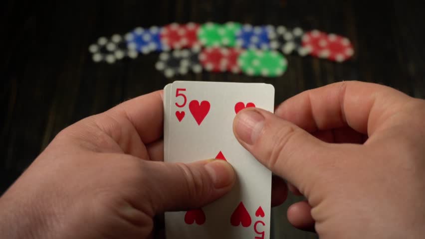 Player holds a hand of playing cards featuring four of a kind or quads, with colorful poker chips arranged on a wooden table in the background, emphasizing the game setting.