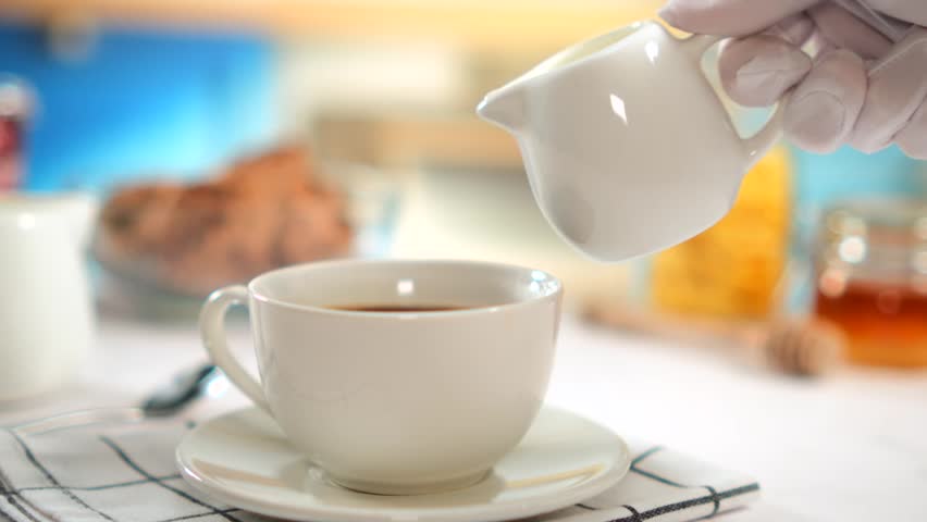 Cream pouring into coffee cup, bright kitchen background, slow motion