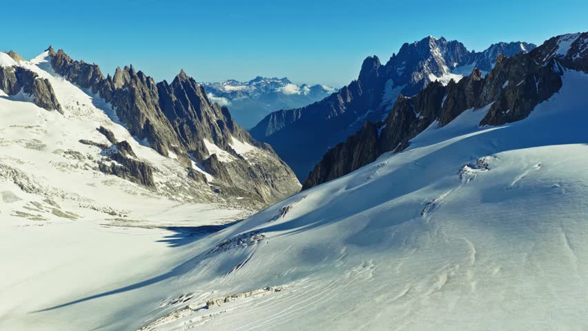 Cinematic aerial view of the French Alps near Chamonix, showing the majestic snow capped peaks and deep valleys of the Mont Blanc massif on a sunny day