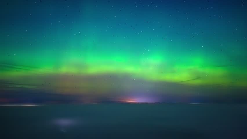 Cinematic drone timelapse of glowing green and purple northern lights moving across dark starry sky above rural winter landscape