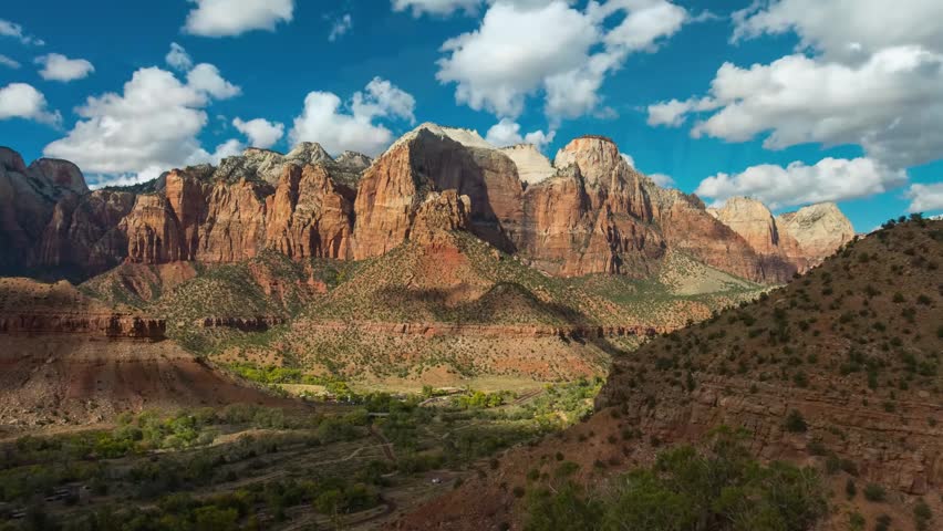 A panoramic shot showcasing the majestic red rock formations and stunning desert landscape of Zion National Park, Utah. The footage captures the iconic Watchman Peak rising prominently above the canyo