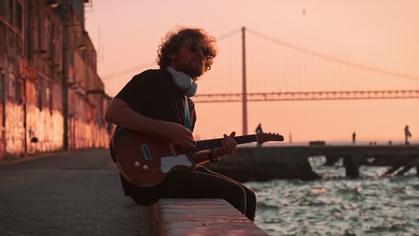 Hipster street musician in black playing electric guitar in the street on sunset