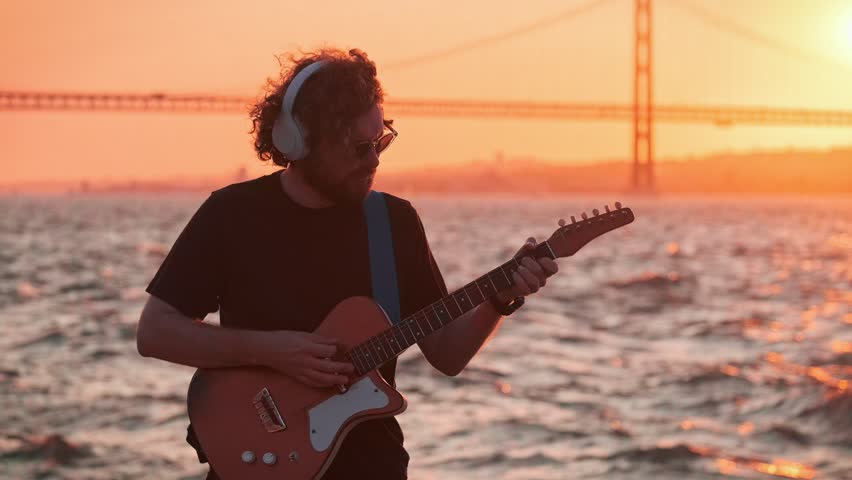 Hipster street musician in black playing electric guitar in street outdoors on sunset
