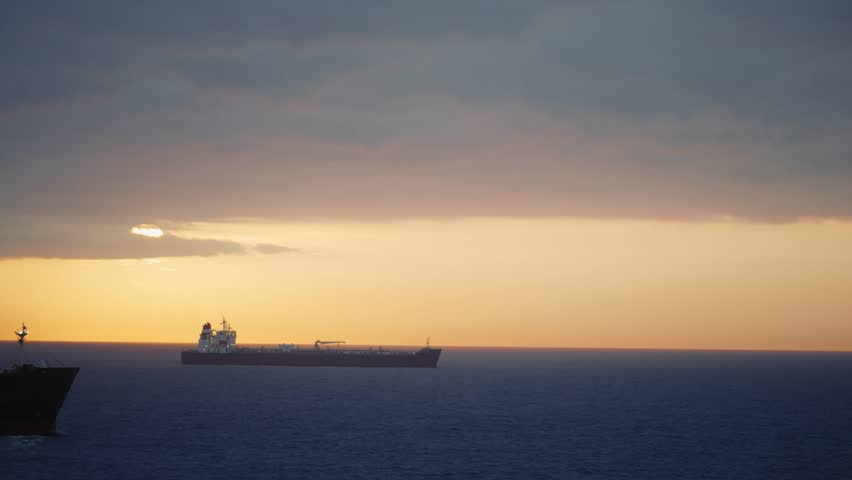 Dawn view of majestic oil tanker sails across the vast Mediterranean Sea, silhouetted against a breathtaking golden sunrise near Barcelona. Global trade meets natural splendor.-