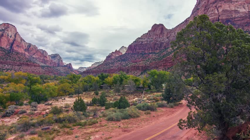 A beautiful, wide-angle view of the iconic Zion Canyon and the Watchman peak in Zion National Park, Utah. The landscape features towering red sandstone cliffs, lush green vegetation in the valley, a w