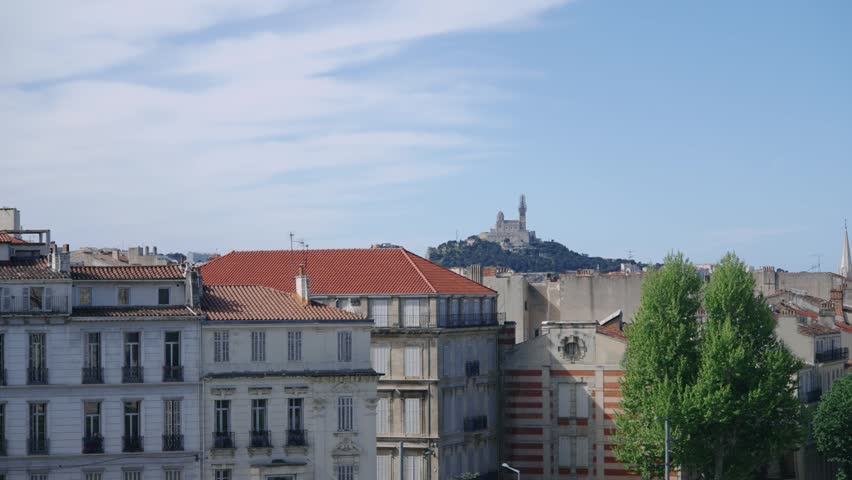 Notre Dame de la Garde basilica majestically overlooking the historic rooftops of vibrant Marseille, France. A beautiful sunny day reveals the city