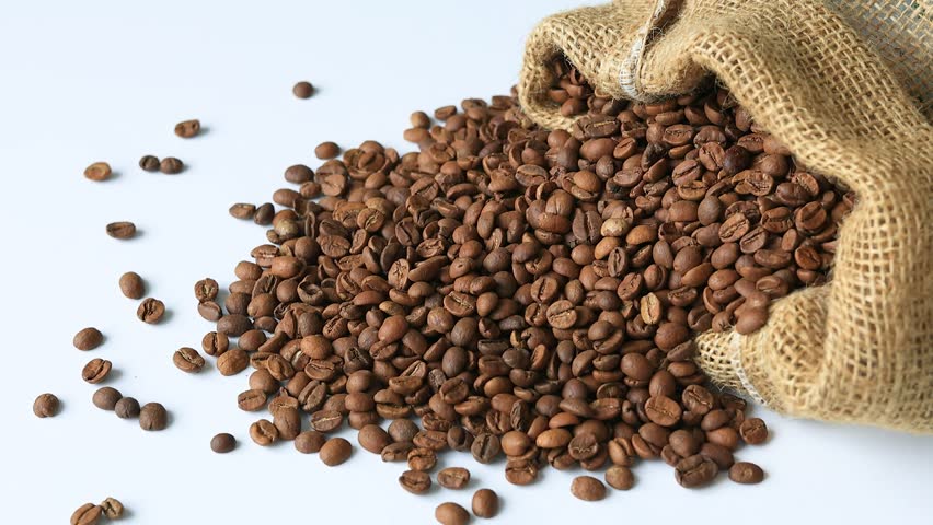 Coffee beans spilled from a linen sack onto a white background