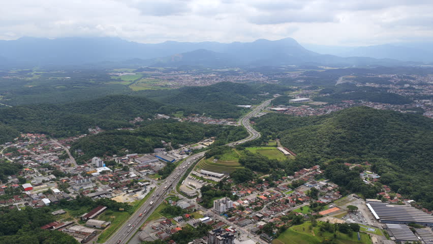 Aerial view of BR-101 highway cutting through Joinville with urban areas, forest and mountains in Brazil.