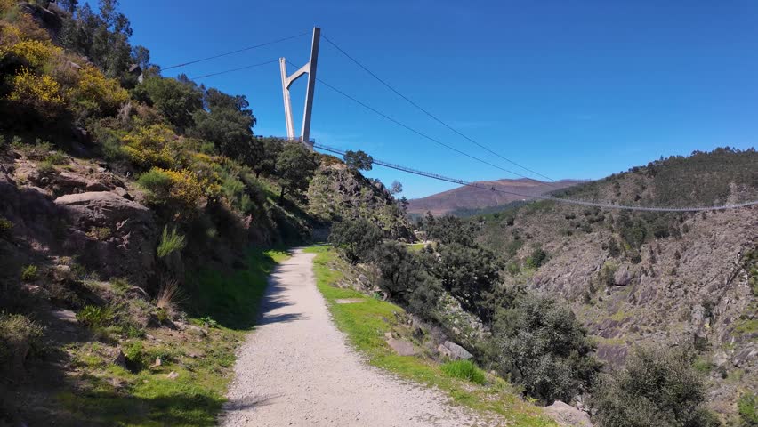 Hiking trail along a deep mountain canyon with a suspension bridge in the background