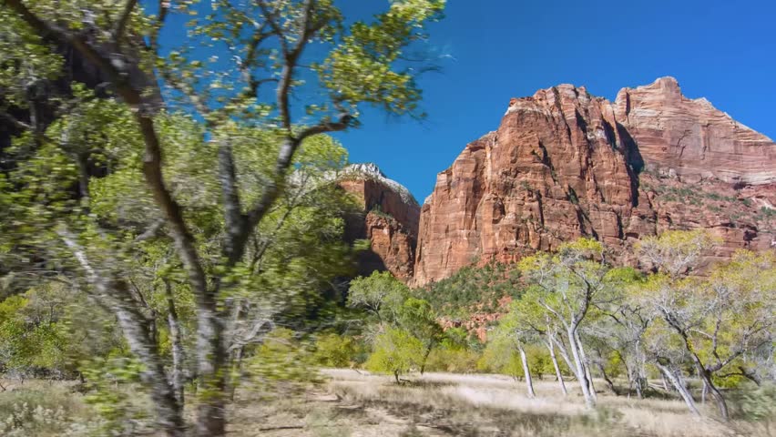 wide-angle view of the iconic landscape within Zion National Park in Utah, USA. The footage captures the massive red sandstone cliffs and rock formations that define the canyon, towering over a lush v