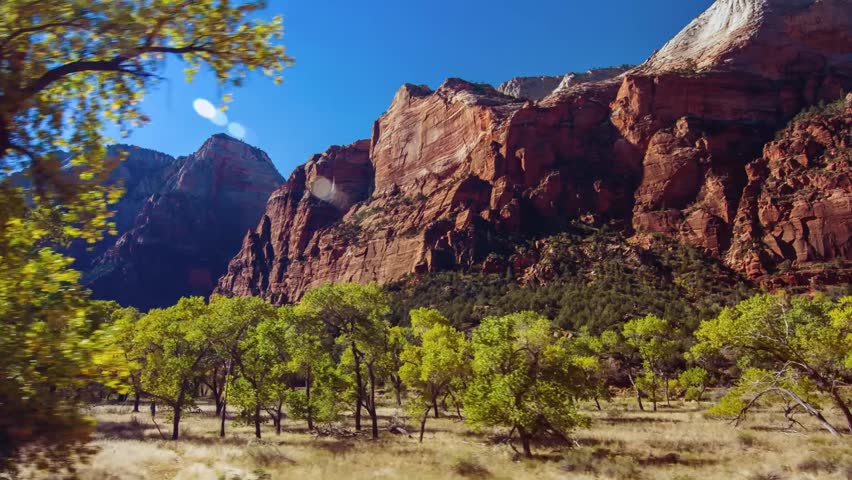 Scenic footage capturing the majestic red and tan-colored Navajo sandstone cliffs of Zion National Park in Utah, USA. The view showcases the dramatic rock formations and the lush green valley floor of