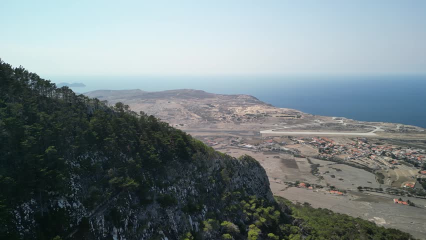 Aerial view of drone flying around Pico do Castelo mountain, with a shape of a vulcano. Porto Santo Island, Madeira, Portugal. Airport and long beach in the background